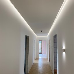Worktime Denys Romanenko - Korytarz z parkietem ułożonym w jodełkę, świeżo pomalowanymi białymi ścianami i sufitem z ukrytym oświetleniem LED. Widoczne surowe ościeżnice drzwi.