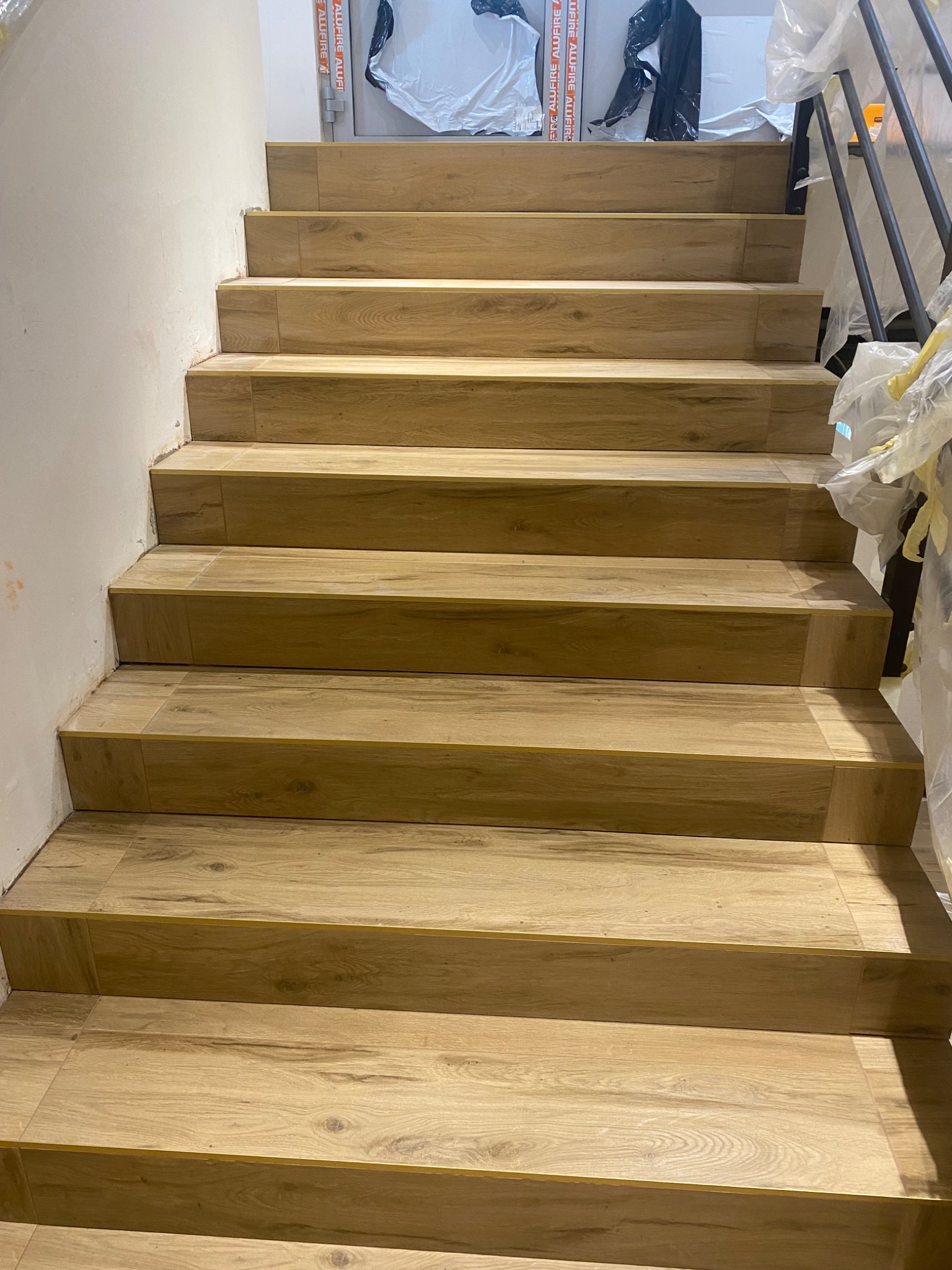 Schody wyłożone panelami imitującymi drewno, widok z dołu, zabezpieczone folią elementy wykończeniowe.