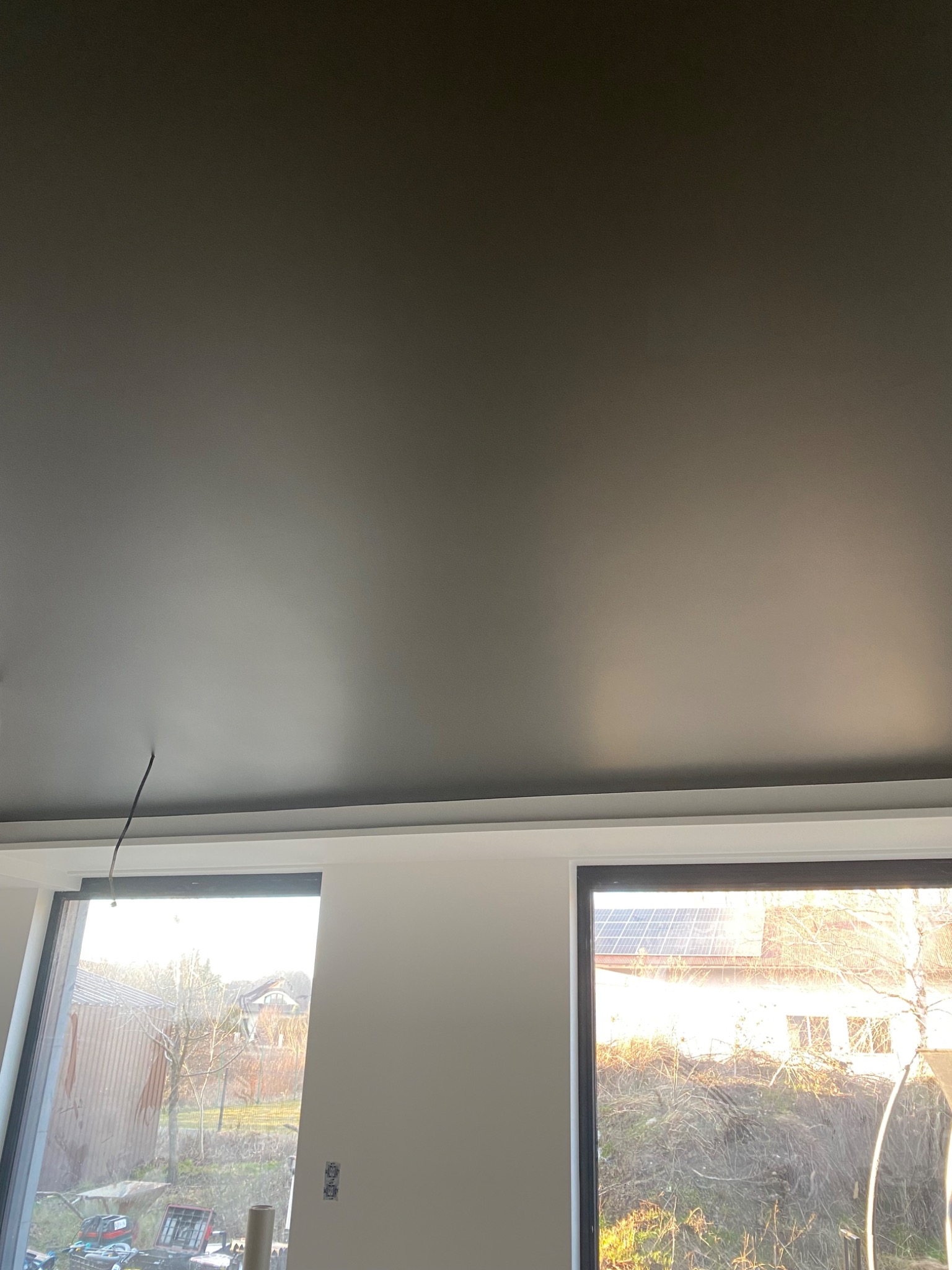 Gładki, ciemnoszary sufit napinany z widocznymi przewodami elektrycznymi, zamontowany w nowym budynku z oknami wychodzącymi na zewnątrz.