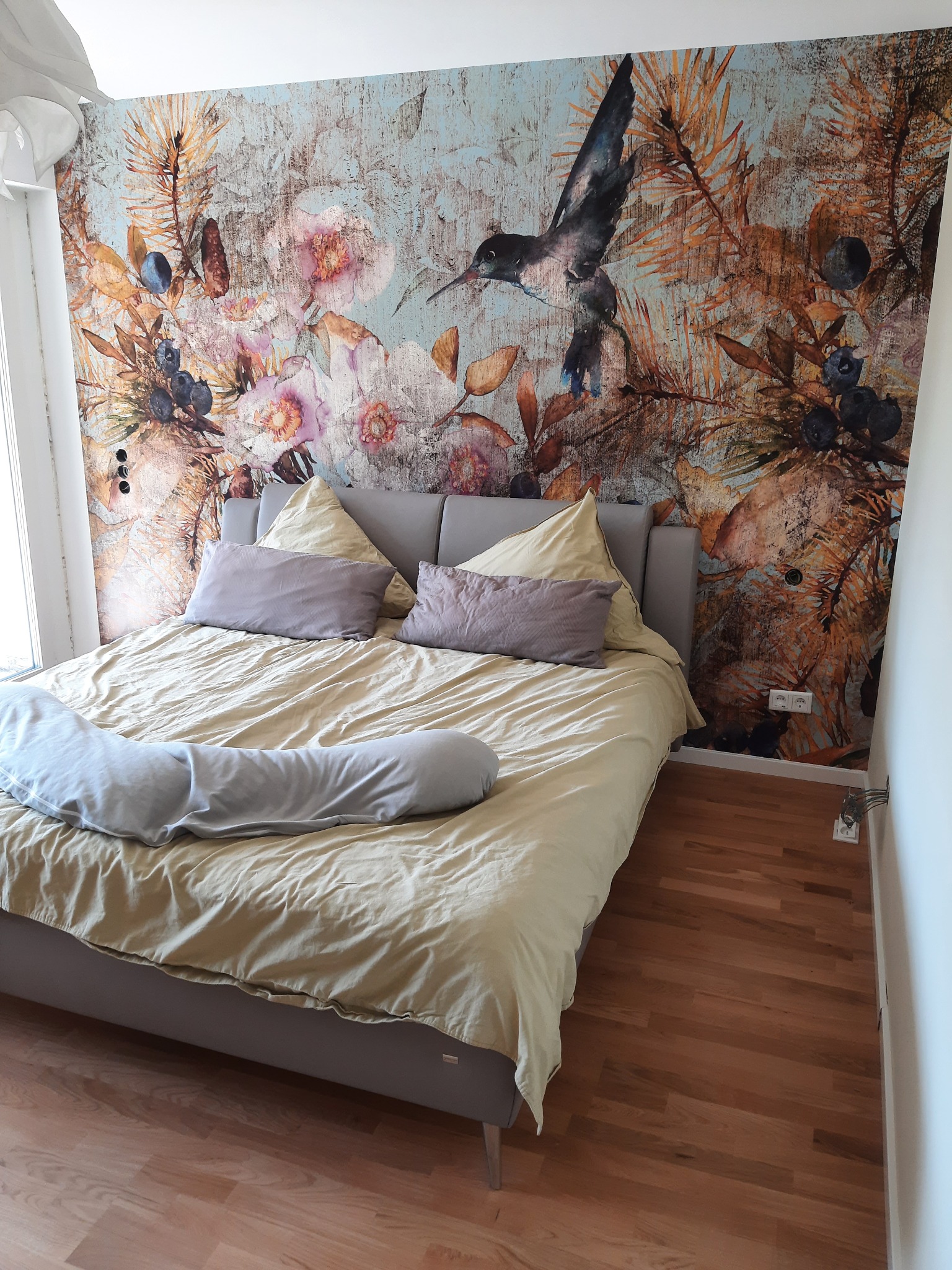 Sypialnia w Sokołowie Małopolskim z łóżkiem na drewnianej podłodze i fototapetą z motywem kwiatów i kolibra na ścianie.