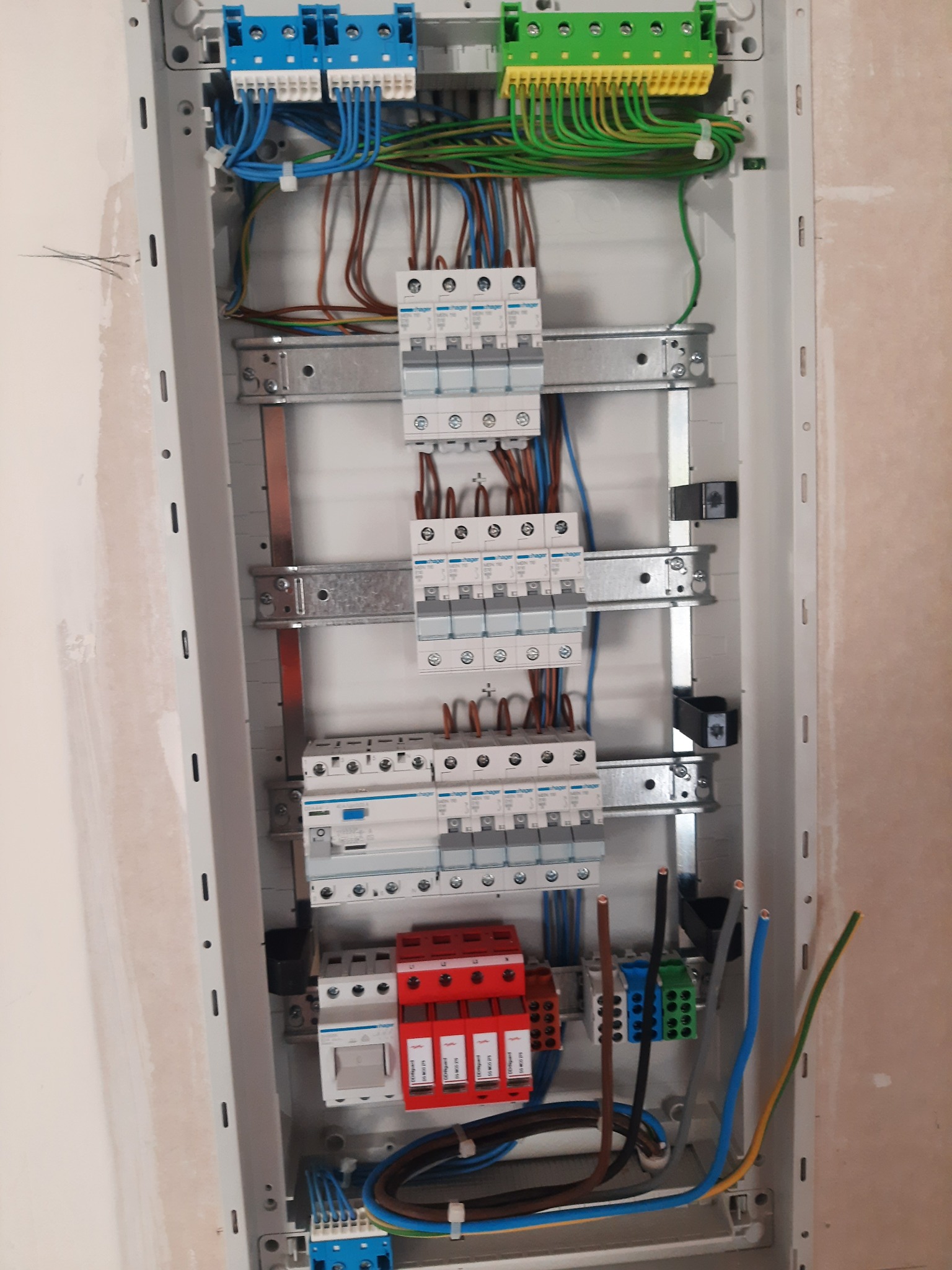 Rozdzielnica elektryczna w trakcie montażu, widoczne zabezpieczenia, przewody w różnych kolorach i listwy zaciskowe, ściana w tle przygotowana do malowania.