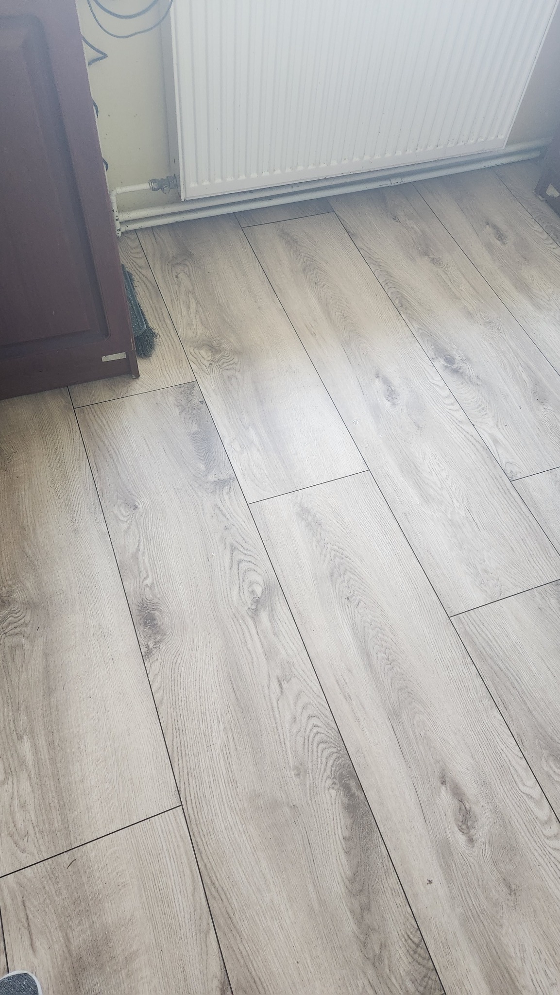 Ułożone panele podłogowe w odcieniach szarości z widocznym grzejnikiem i fragmentem brązowych drzwi.