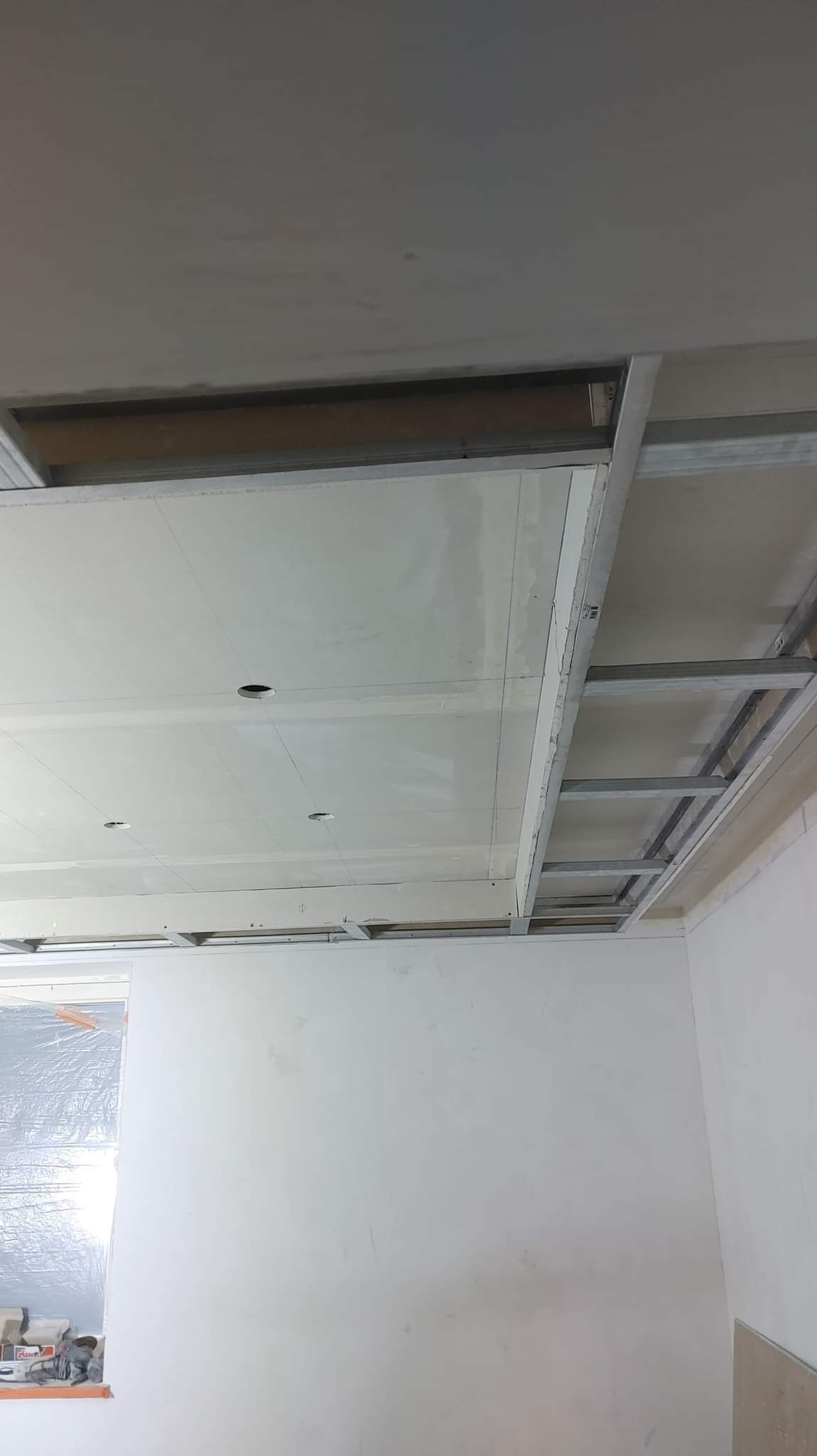 Stelaż metalowy podwieszanego sufitu z płyt gipsowo-kartonowych, widoczne otwory na oświetlenie punktowe, stan surowy przed wykończeniem.