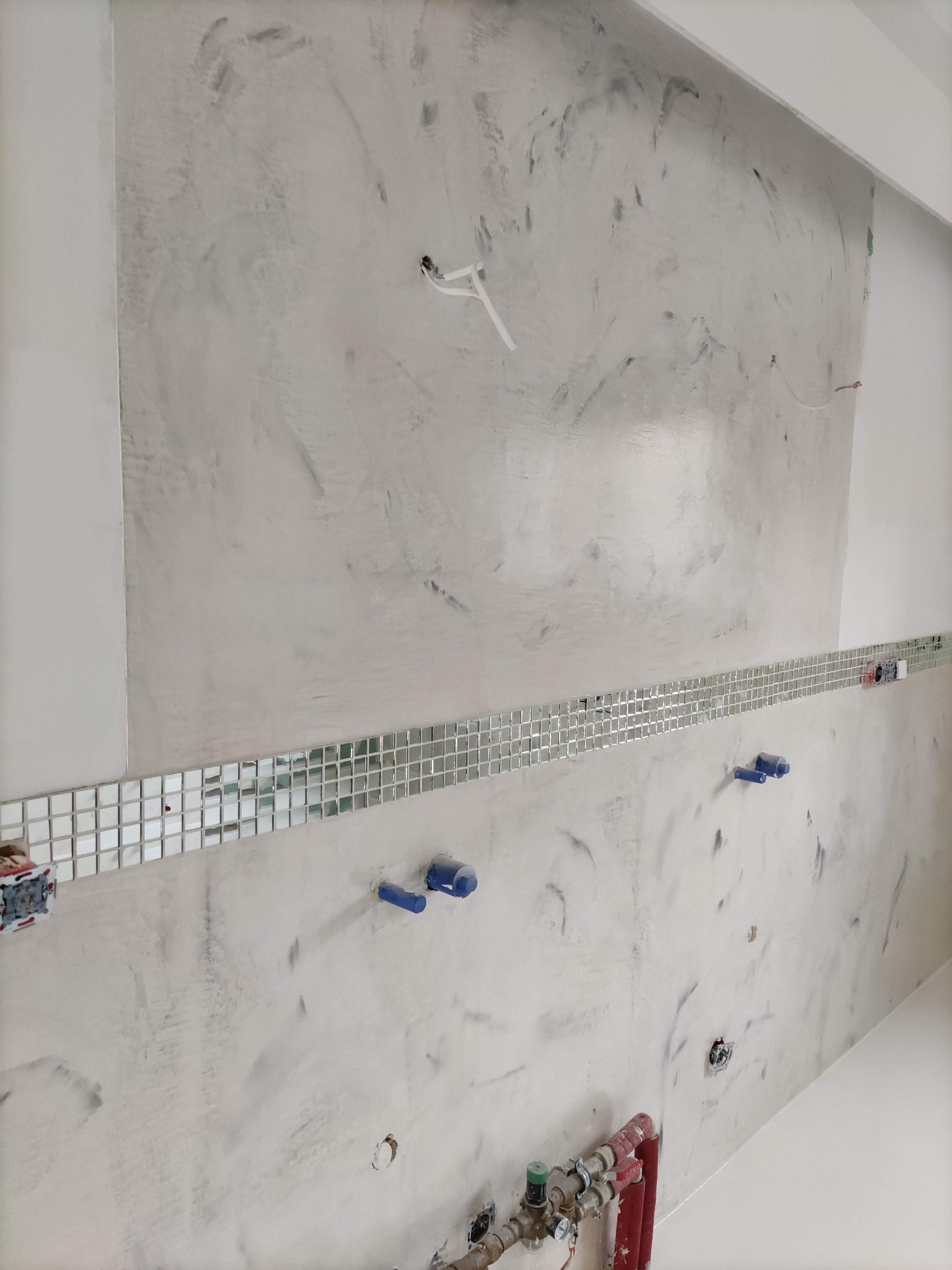 Ściana po nałożeniu dekoracyjnej warstwy imitującej marmur, z poziomym pasem mozaiki lustrzanej i wystającymi elementami instalacji wodnej i elektrycznej.