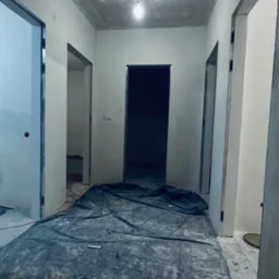 Korytarz w trakcie remontu: sufit z płyt kartonowo-gipsowych po szpachlowaniu, podłoga zabezpieczona folią malarską, widoczne ościeżnice drzwiowe przed malowaniem.