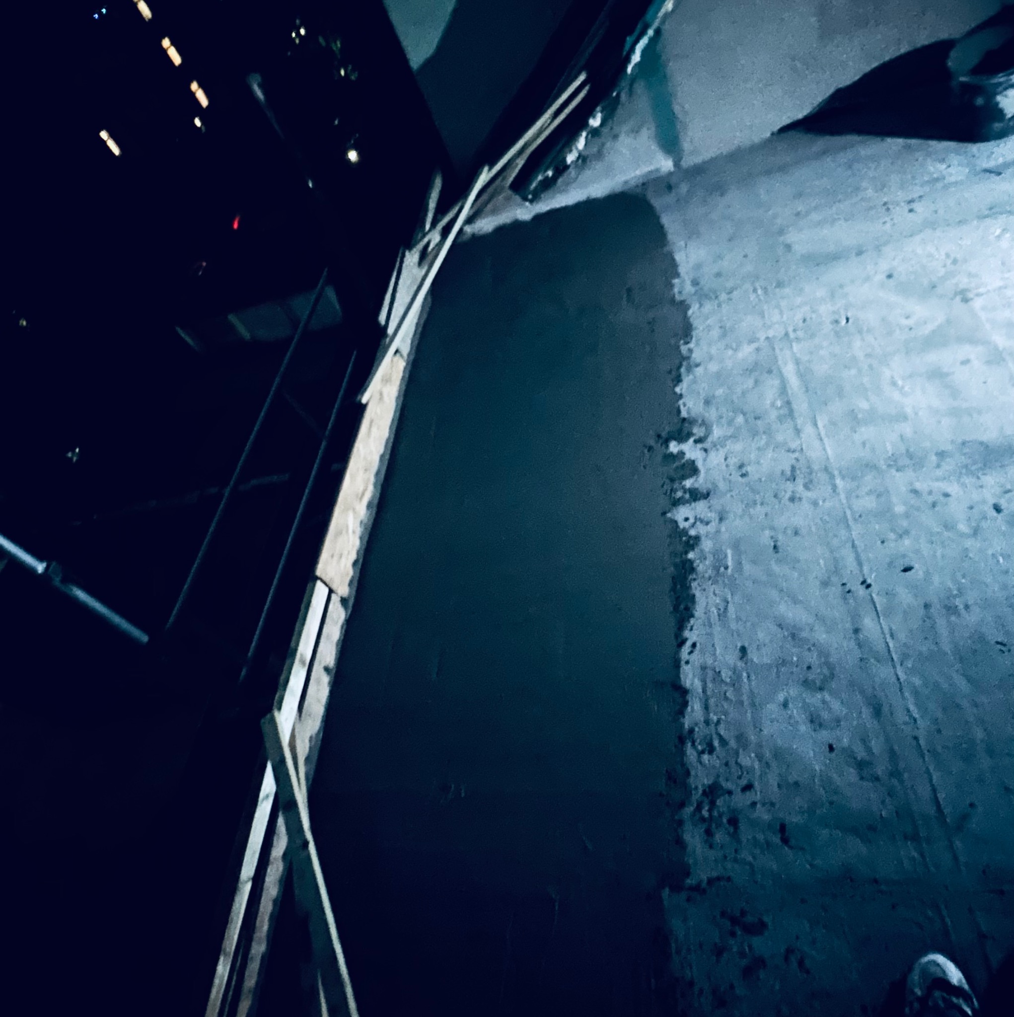 Ściana w trakcie szpachlowania z widocznym rusztowaniem i fragmentem starej powierzchni, oświetlona w ciemnym pomieszczeniu.