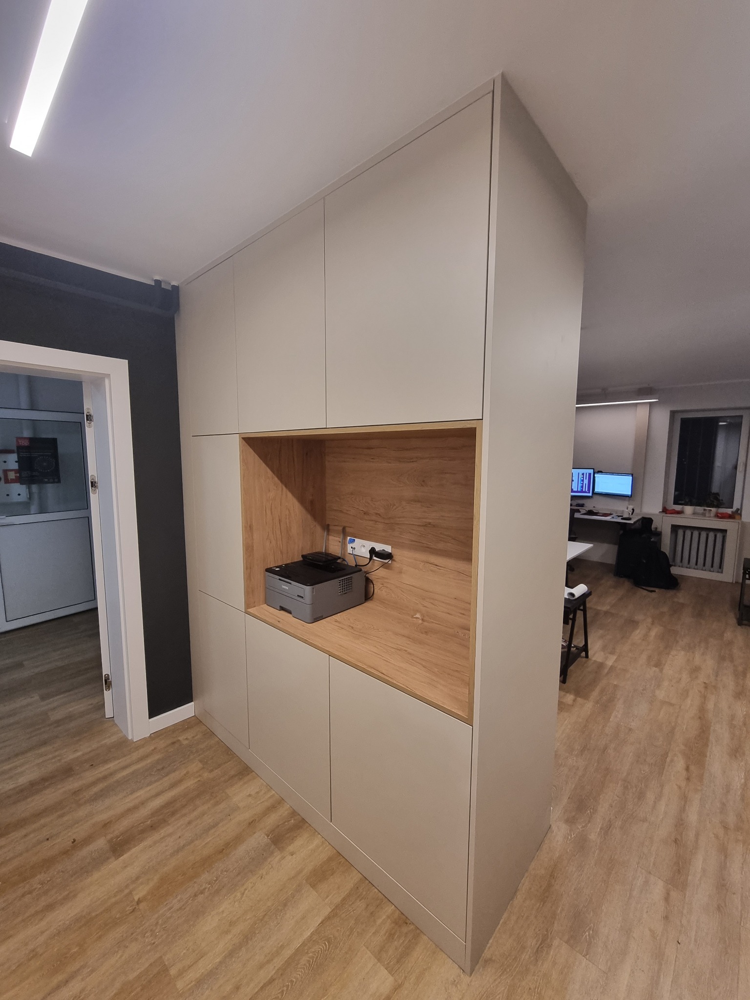 Biała szafa na wymiar z drewnianą wnęką, w której znajduje się drukarka, widok z boku w biurze.