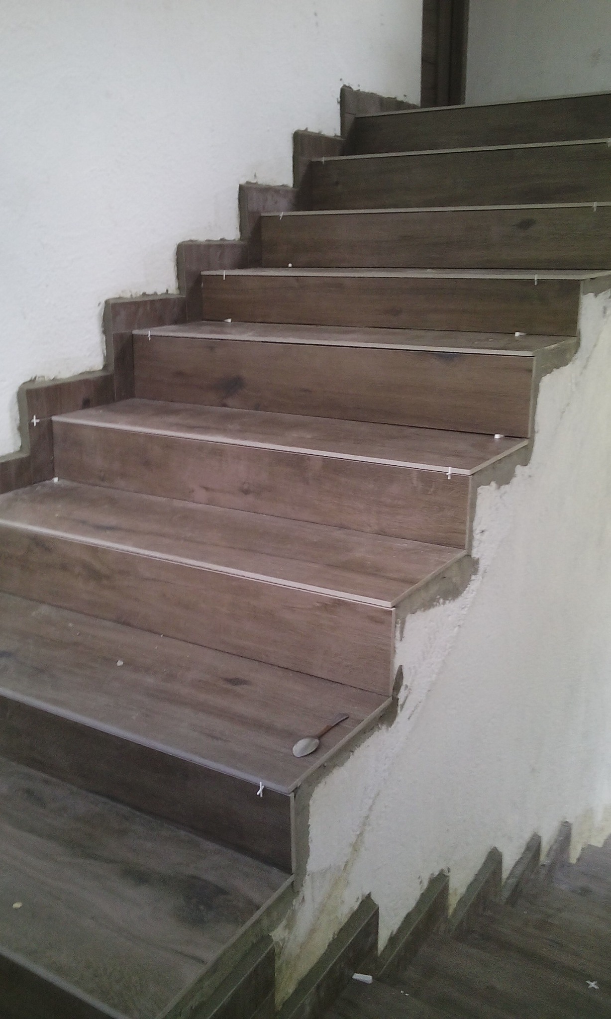 Schody wyłożone brązowymi płytkami imitującymi drewno, z widocznymi krzyżykami dystansowymi i śladami zaprawy, łyżeczka na jednym ze stopni.