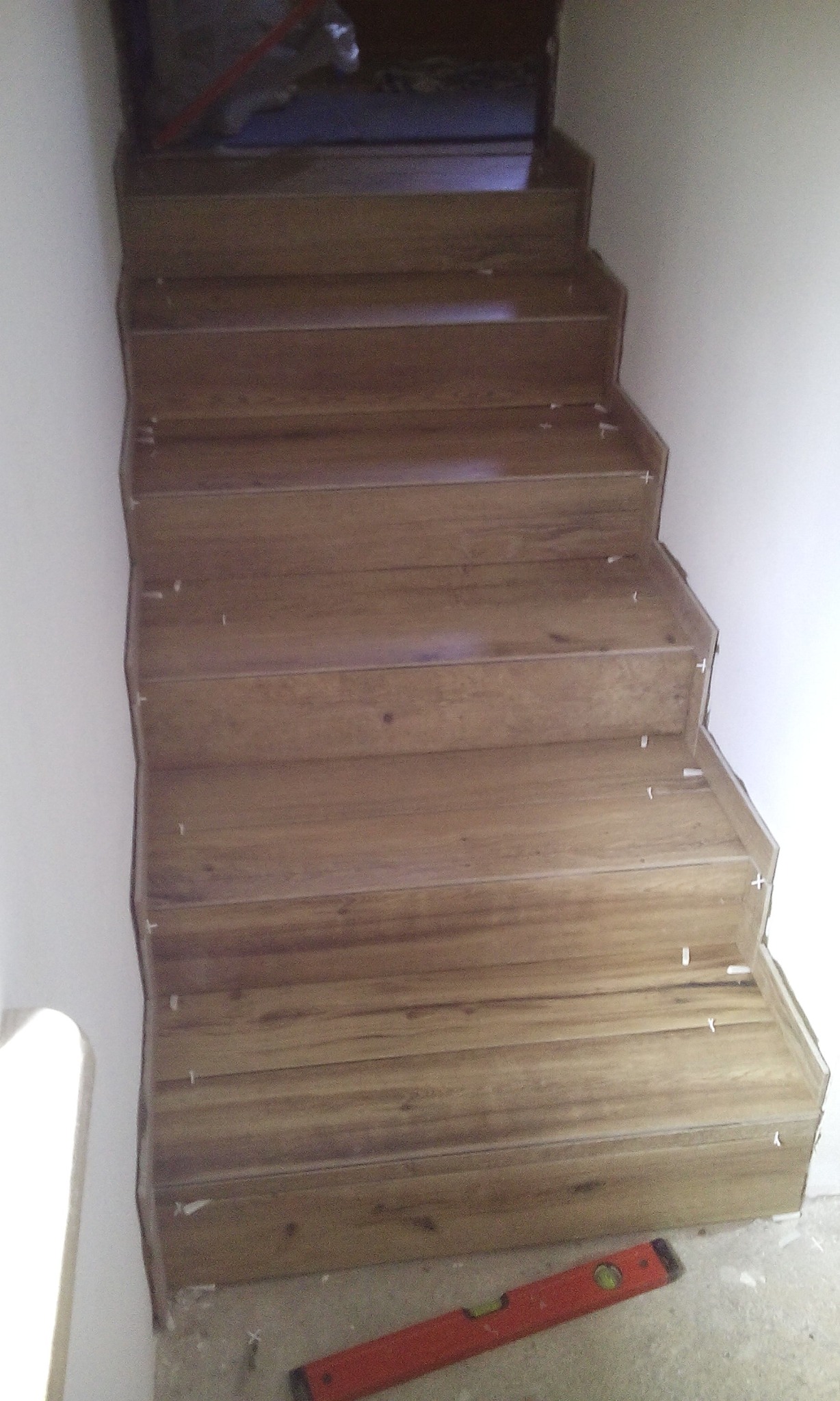 Montaż drewnopodobnych płytek na schodach wewnętrznych, widoczne krzyżyki dystansowe i poziomica na podłodze.