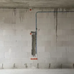 Surowa ściana z betonu komórkowego z widocznymi przewodami elektrycznymi w peszlach i puszkami instalacyjnymi, częściowo zamaskowanymi zaprawą, w trakcie prac instalacyjnych.