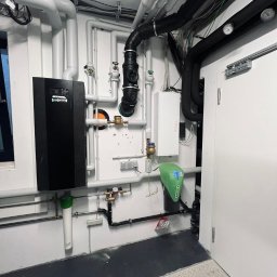 Andrzej Gmachowski - Zainstalowany piec gazowy Viessmann z rozbudowaną instalacją hydrauliczną, widoczne rury w kolorze białym i czarnym, filtry wody i manometry na ścianie w pomieszczeniu technicznym.