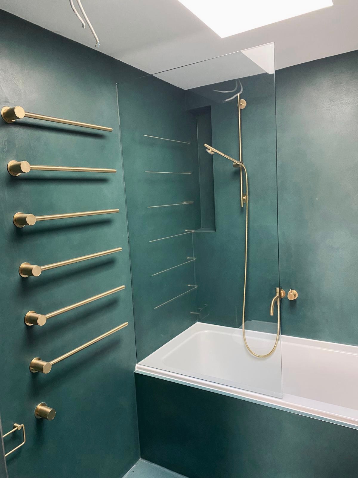 Nowoczesna łazienka z zielonymi ścianami, złotą armaturą i grzejnikiem drabinkowym, minimalistyczny design.