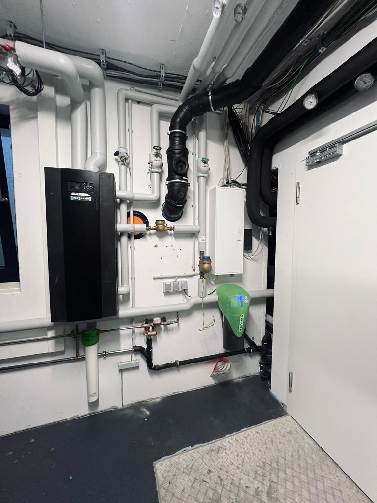 Zainstalowany piec gazowy Viessmann z rozbudowaną instalacją hydrauliczną, widoczne rury w kolorze białym i czarnym, filtry wody i manometry na ścianie w pomieszczeniu technicznym.