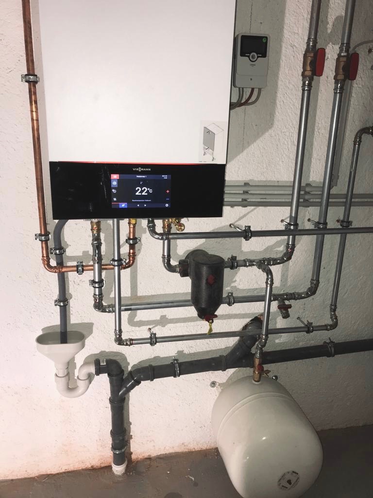 Nowoczesny piec gazowy Viessmann z wyświetlaczem ustawionym na 22 stopnie Celsjusza, widoczne rury miedziane i stalowe, biały zbiornik wyrównawczy i syfon pod umywalkę