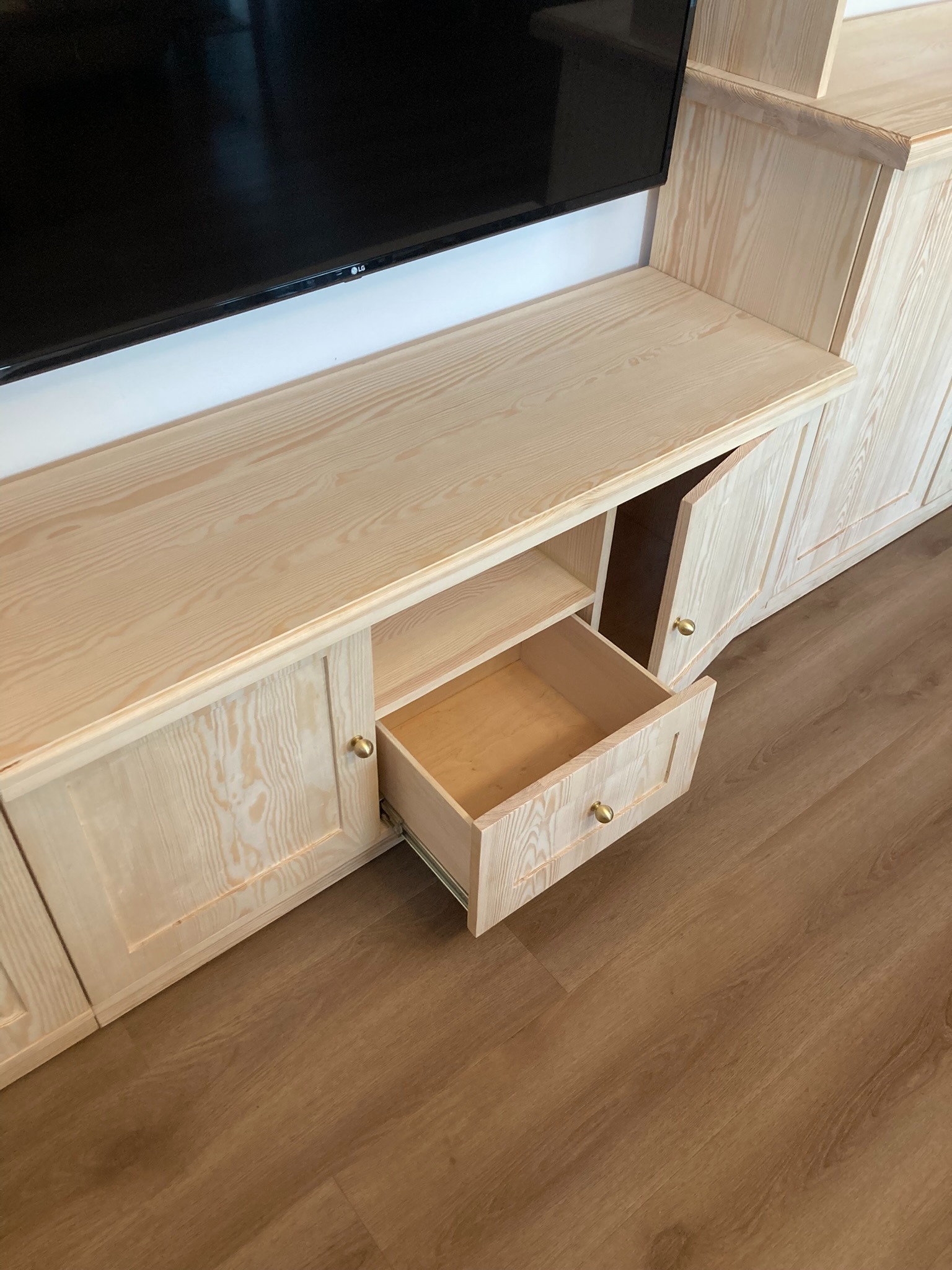 Jasna, drewniana szafa na wymiar z wysuwaną szufladą i telewizorem na górze, widoczna faktura drewna.