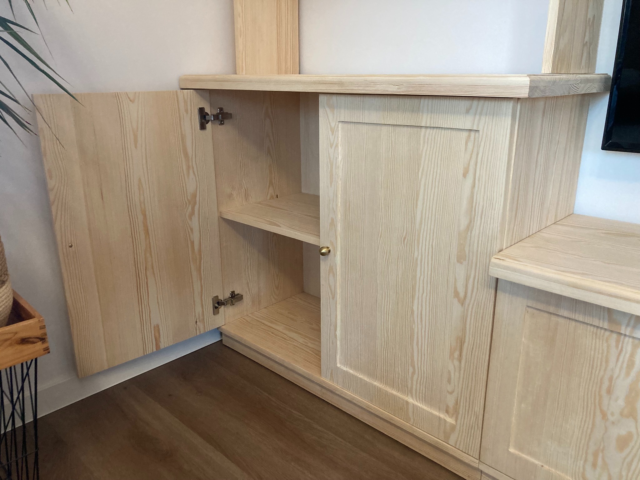 Jasna, drewniana zabudowa meblowa z otwartą szafką, widoczne półki wewnątrz i zawiasy mocujące drzwi.
