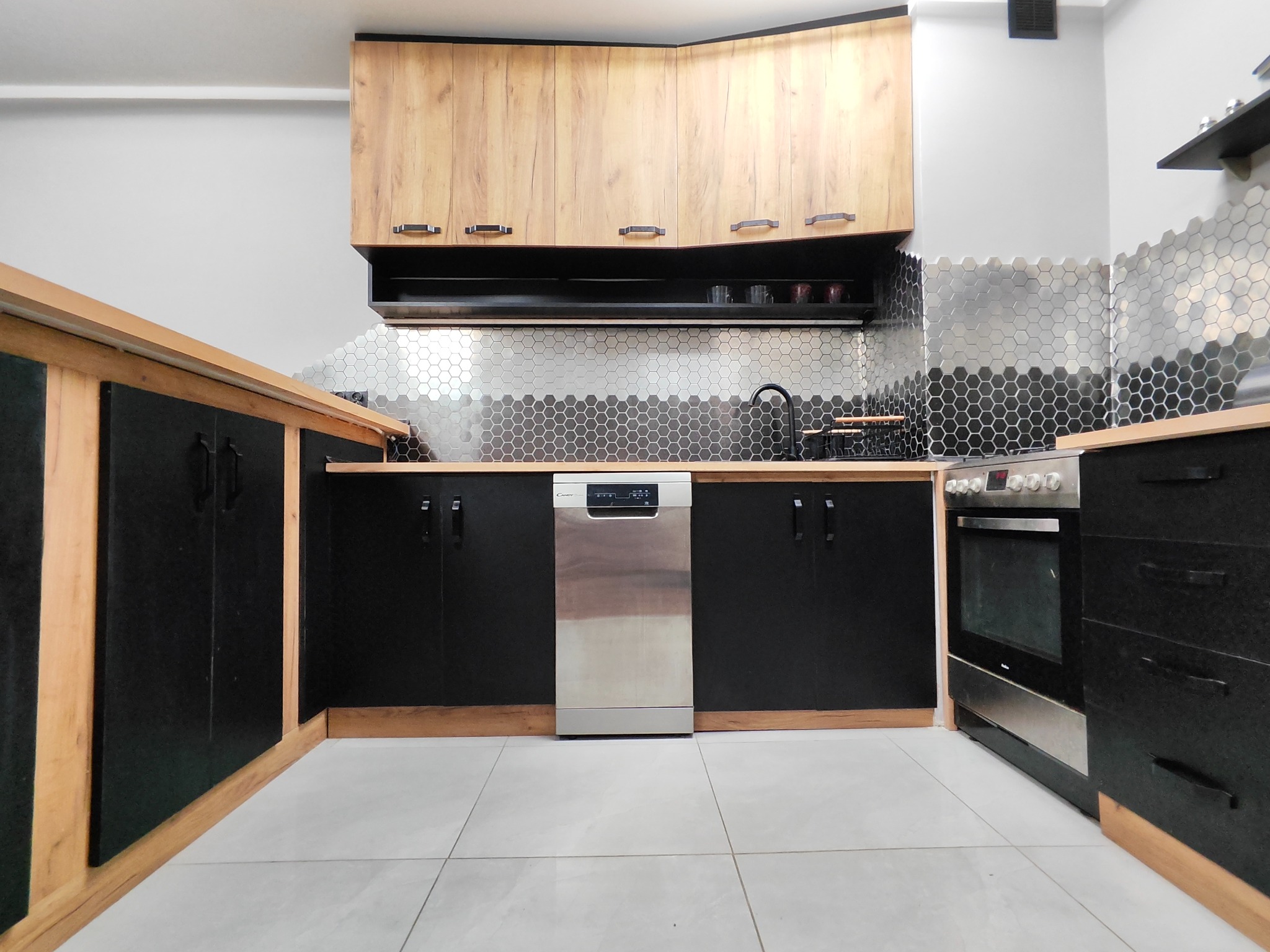 Nowoczesna kuchnia z górnymi szafkami w odcieniach drewna, dolnymi szafkami w kolorze czarnym, srebrną mozaiką na ścianie i srebrną zmywarką.