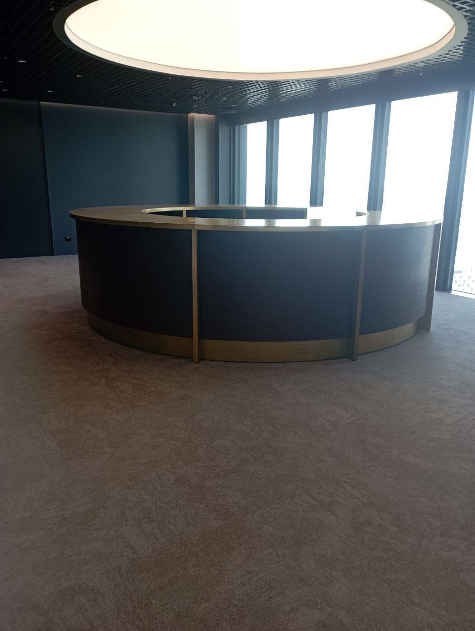 Okrągła lada recepcyjna z ciemnego drewna z metalowymi akcentami w nowoczesnym biurze w Warszawie, oświetlona okrągłym plafonem.