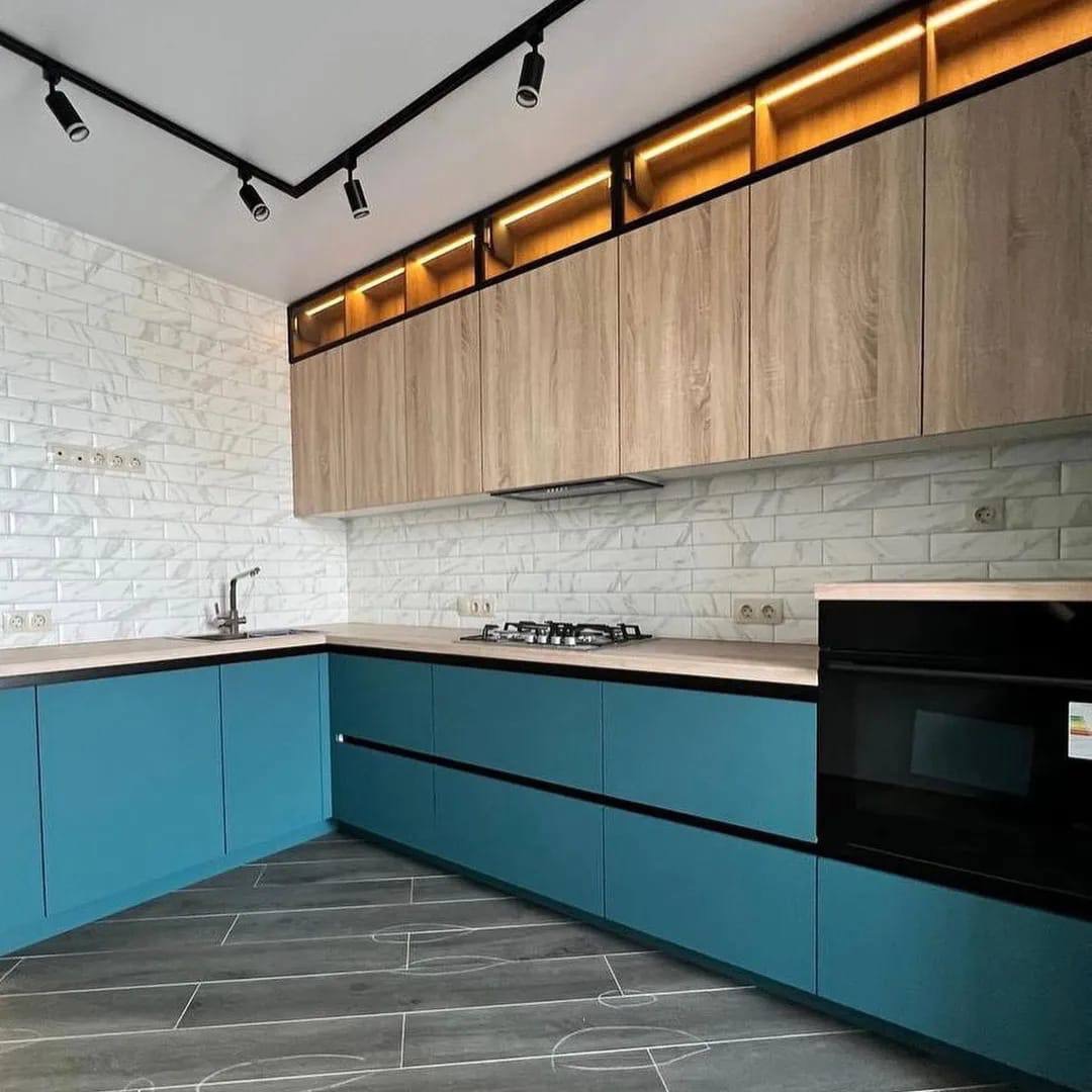 Nowoczesna kuchnia z turkusowymi szafkami dolnymi i drewnopodobnymi górnymi, oświetlenie LED pod szafkami górnymi, biała ceglana ściana nad blatem, szare panele podłogowe imitujące drewno.
