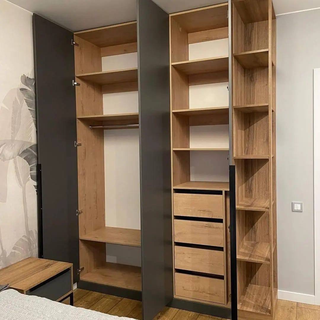 Otwarty, nowoczesny system szaf wnękowych z szarymi drzwiami i drewnianymi półkami oraz szufladami w sypialni z wzorzystą tapetą.