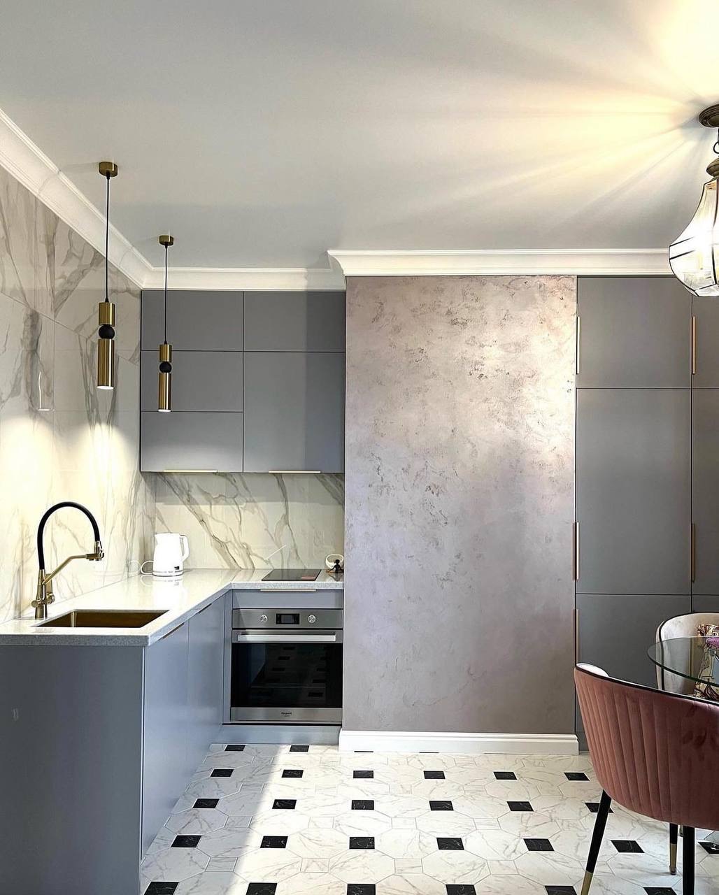 Nowoczesna kuchnia w odcieniach szarości z marmurowym backsplashiem, złotymi akcentami w postaci lamp i baterii, oraz geometryczną podłogą w biało-czarne wzory.
