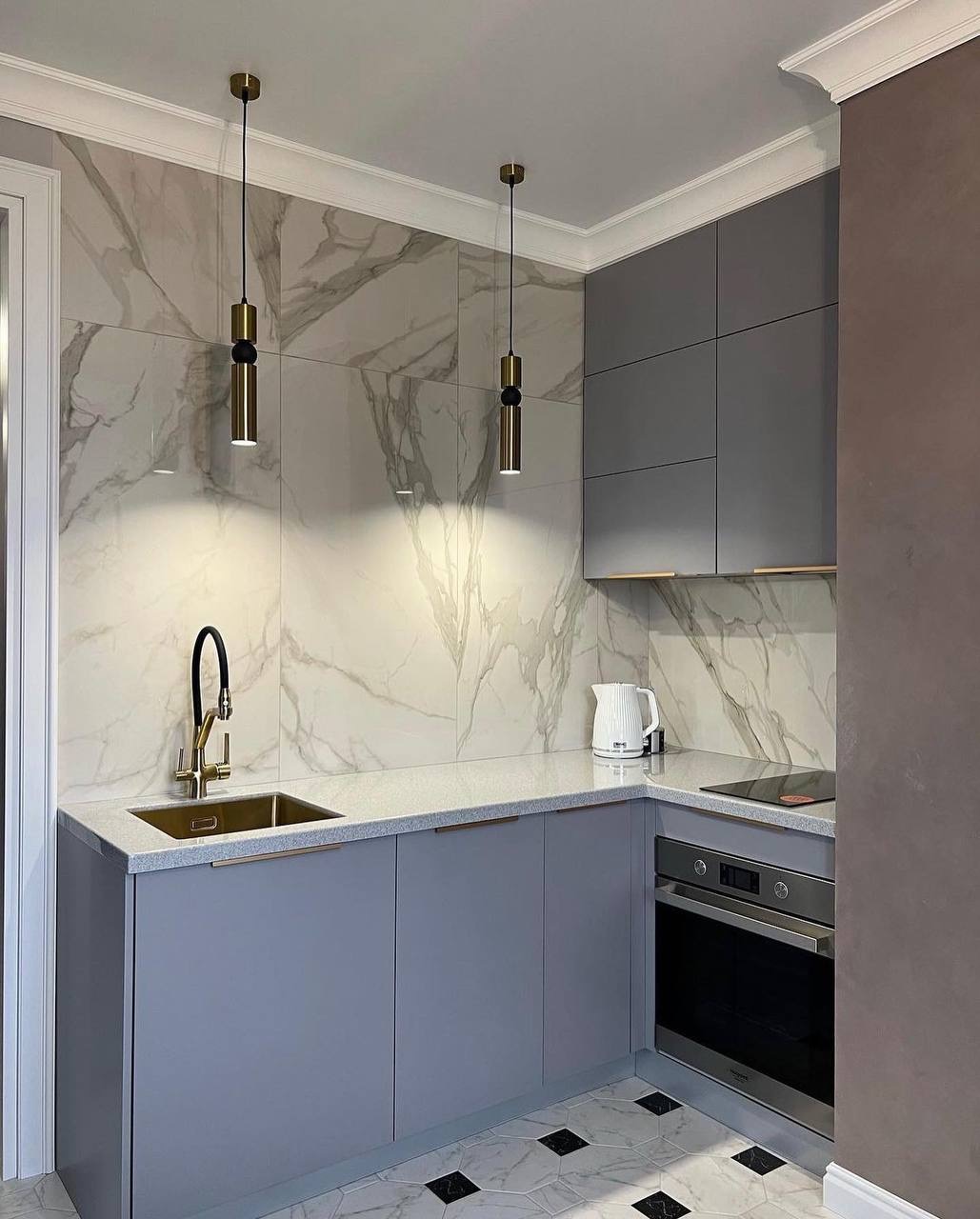 Nowoczesna kuchnia w odcieniach szarości z marmurowymi płytkami, złotą armaturą i geometryczną podłogą, oświetlona wiszącymi lampami.