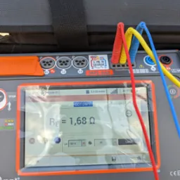Miernik elektryczny Sonel MPI-540 z podłączonymi przewodami pomiarowymi (czerwony, żółty, niebieski) wyświetlający wynik pomiaru rezystancji uziemienia 1,68 Ω. Ekran urządzenia zabezpieczony folią...