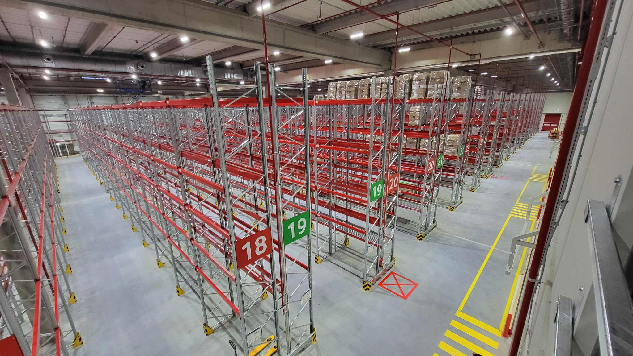 Wnętrze nowego magazynu logistycznego z wysokimi regałami paletowymi, oznaczonymi numerami 18, 19 i 20, gotowe do składowania towarów.