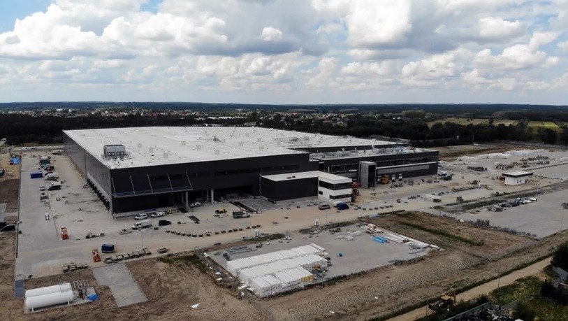 Rozległy widok z lotu ptaka na budowę centrum dystrybucyjnego LIDL, pokazujący postęp prac, z widocznymi elementami konstrukcyjnymi, placem budowy i otaczającym terenem.