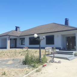 MK Fenster - Maciej Kaszczyk @oknamaciek - Parterowy dom jednorodzinny z ciemnymi żaluzjami zewnętrznymi, widok z przodu na ogród z lampą i hulajnogą.