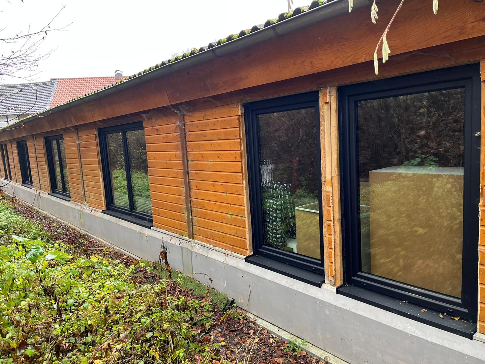 Budynek z drewnianą elewacją i rzędem czarnych okien, widok z zewnątrz, widoczne elementy montażowe przy oknach.