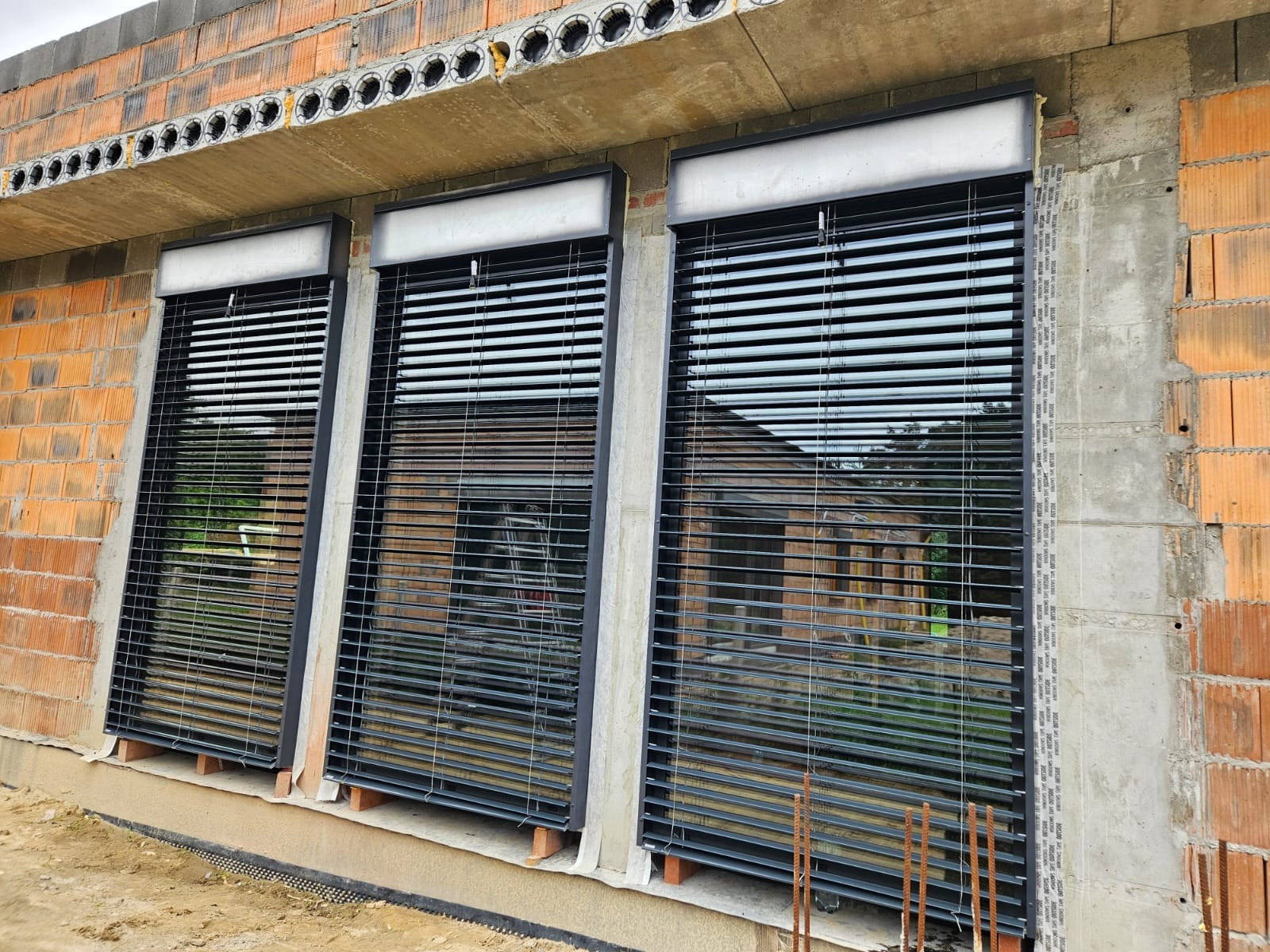 Montaż żaluzji fasadowych w nowo budowanym domu w Poznaniu, widoczne surowe mury z cegły i betonowe nadproże.