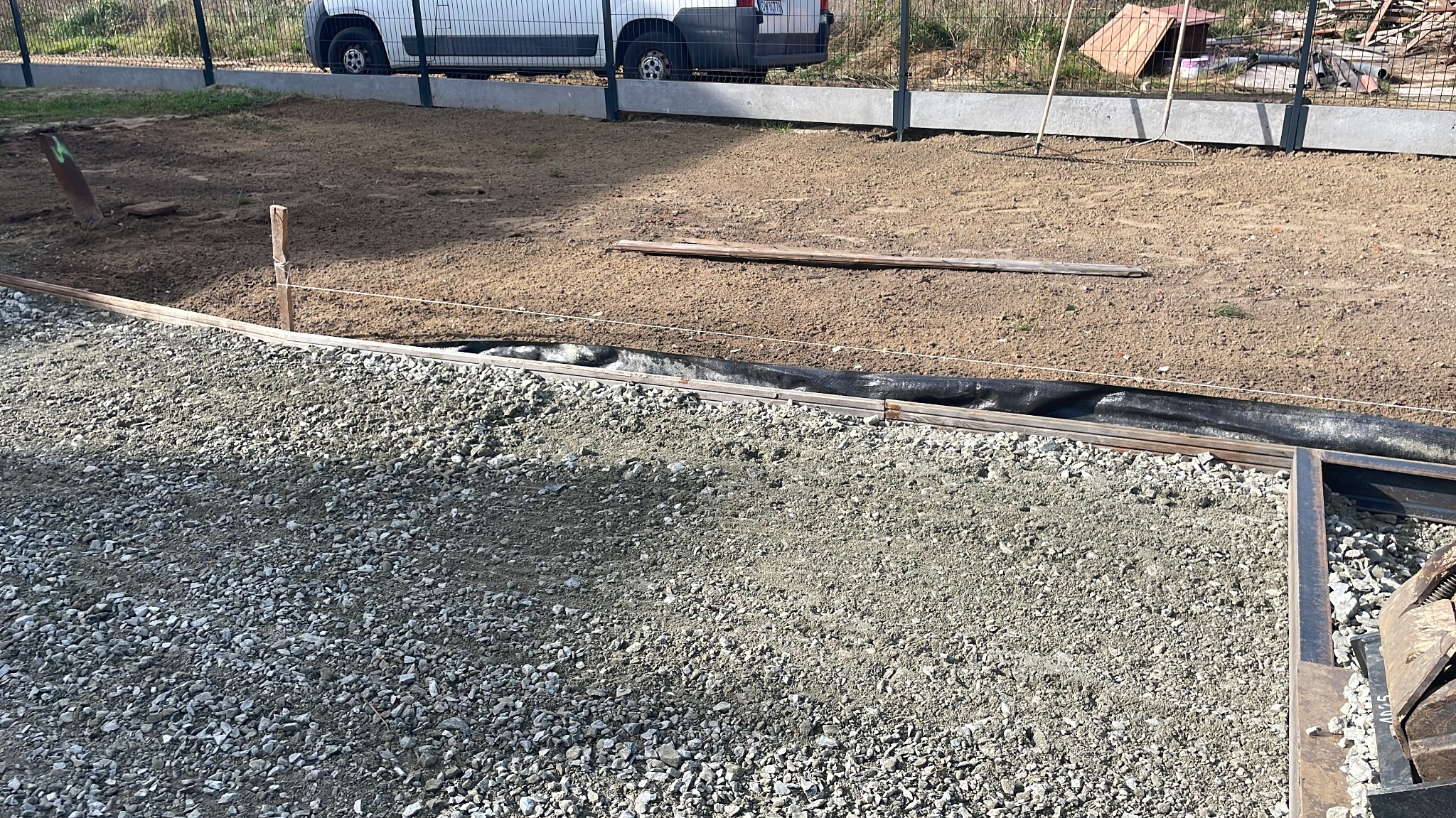 Przygotowanie podłoża pod drogę: warstwa tłucznia, geowłóknina i wytyczone granice, w tle wyrównany teren i zaparkowany bus.