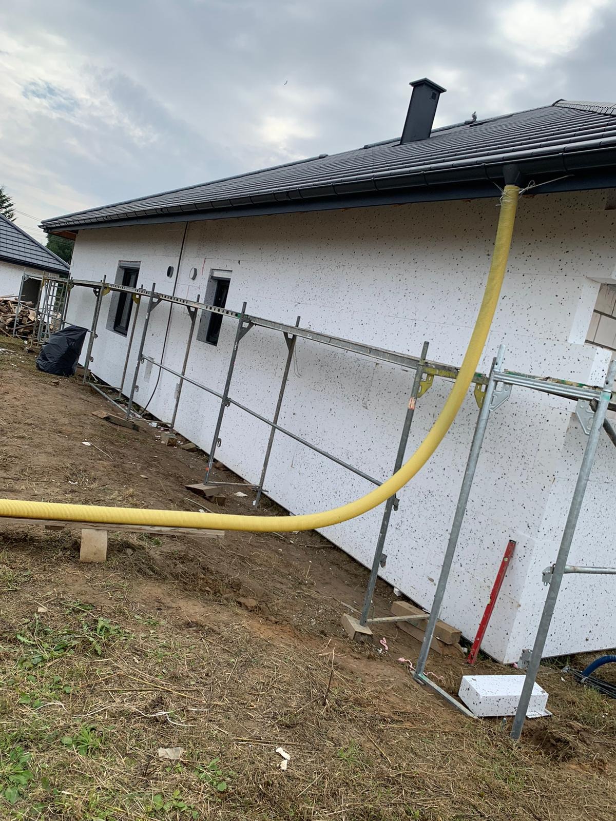 Dom jednorodzinny w trakcie prac wykończeniowych elewacji, widoczne rusztowania, żółty wąż wentylacyjny i styropian z fakturą baranka.