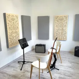 Pokój do ćwiczeń muzycznych z panelami akustycznymi na ścianach, wzmacniaczami Fender, statywem na nuty i gitarą na stojaku, przygotowany do zajęć.
