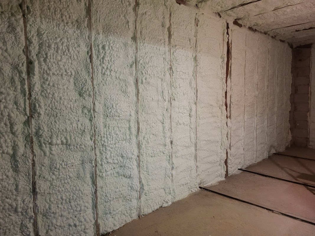 Poddasze po aplikacji izolacji pianką PUR, widoczne drewniane elementy konstrukcyjne. Biała, spieniona struktura pokrywa ściany i sufit.