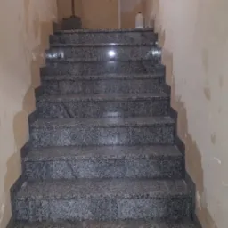 Schody wyłożone szarym, nakrapianym granitem, z widocznymi śladami świeżo położonych gładzi na ścianach w klatce schodowej.