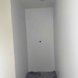 VIRA-BUD SVITLANA MALYSHENKO - Wnętrze po malowaniu na biało, zabezpieczona podłoga folią malarską. Widoczne gładkie ściany i sufit, oświetlenie. Minimalistyczny efekt końcowy.