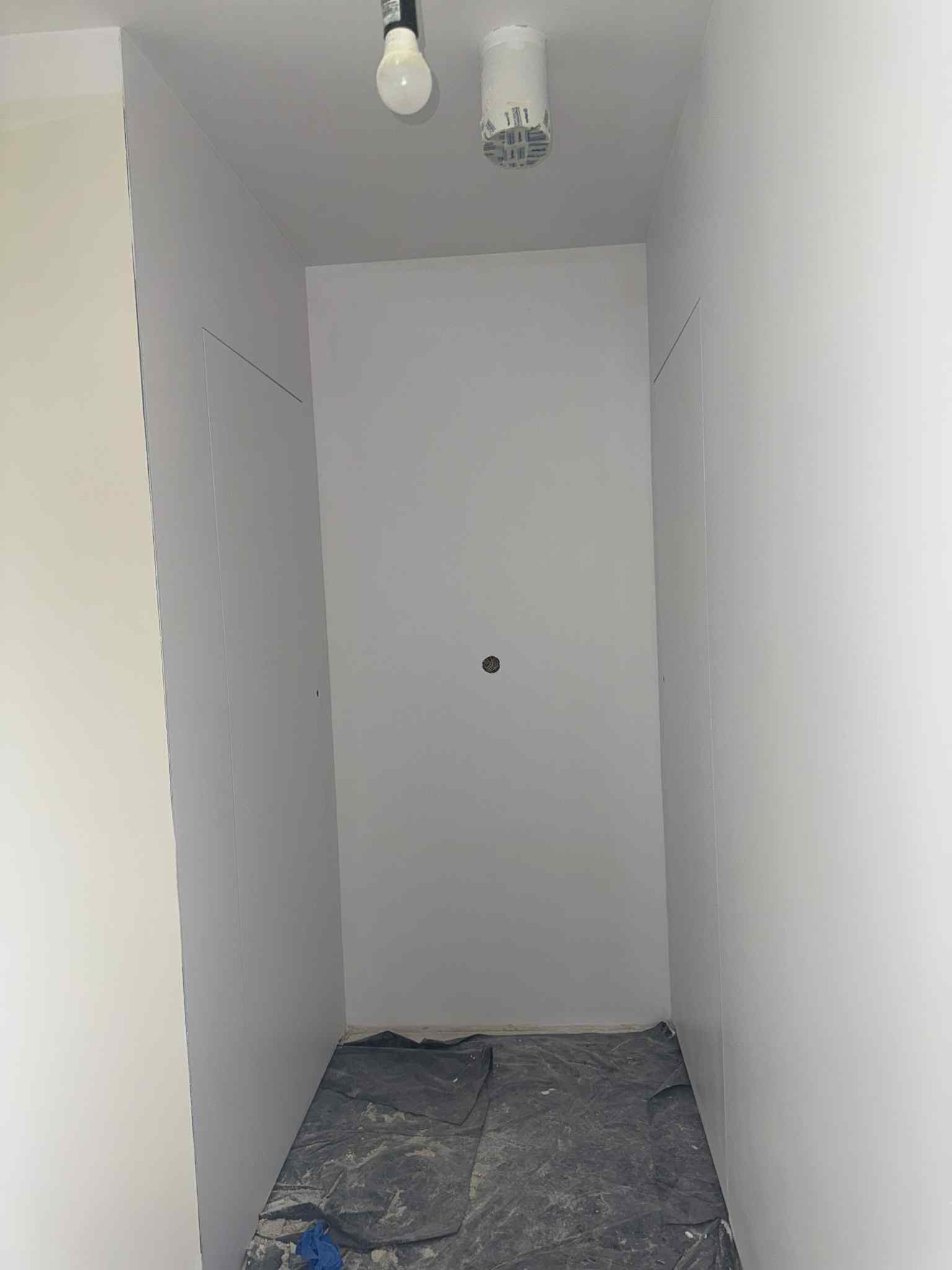 Wnętrze po malowaniu na biało, zabezpieczona podłoga folią malarską. Widoczne gładkie ściany i sufit, oświetlenie. Minimalistyczny efekt końcowy.