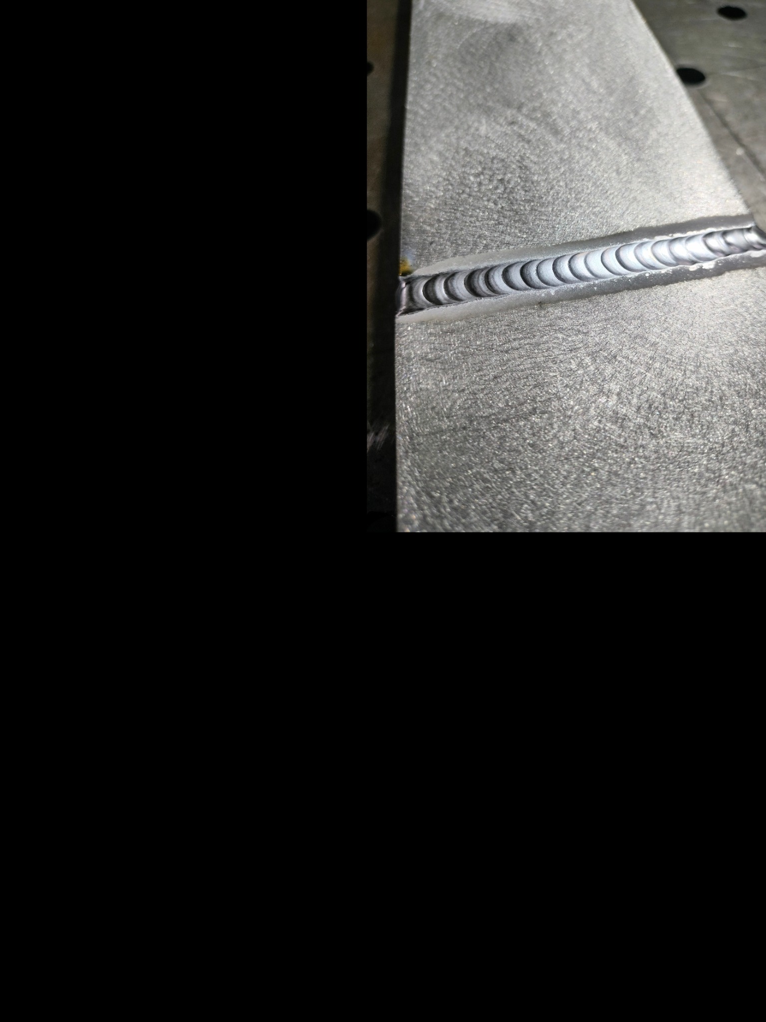 Szlifowana powierzchnia metalowa z precyzyjnym spoiną łukową, widoczne regularne ślady po spawaniu.