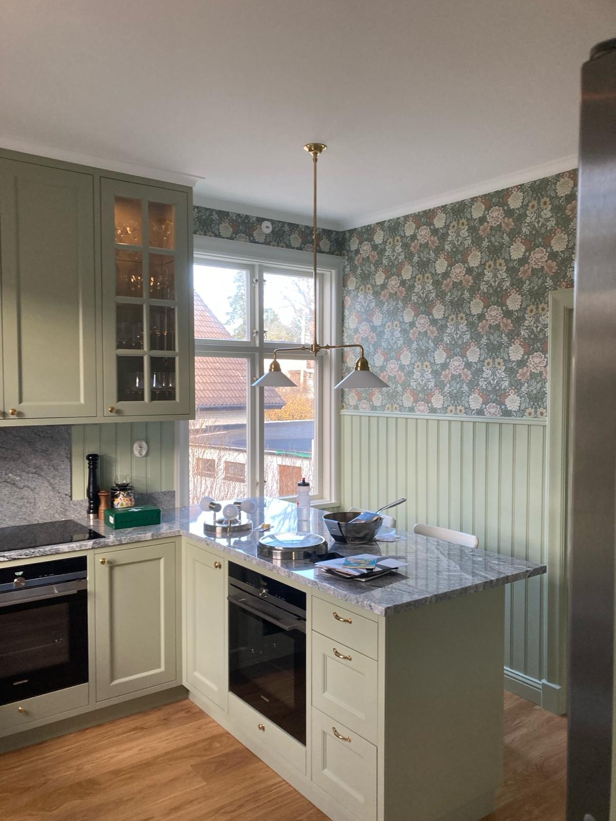 Jasna kuchnia w stylu retro z wyspą, marmurowym blatem i kwiecistą tapetą.