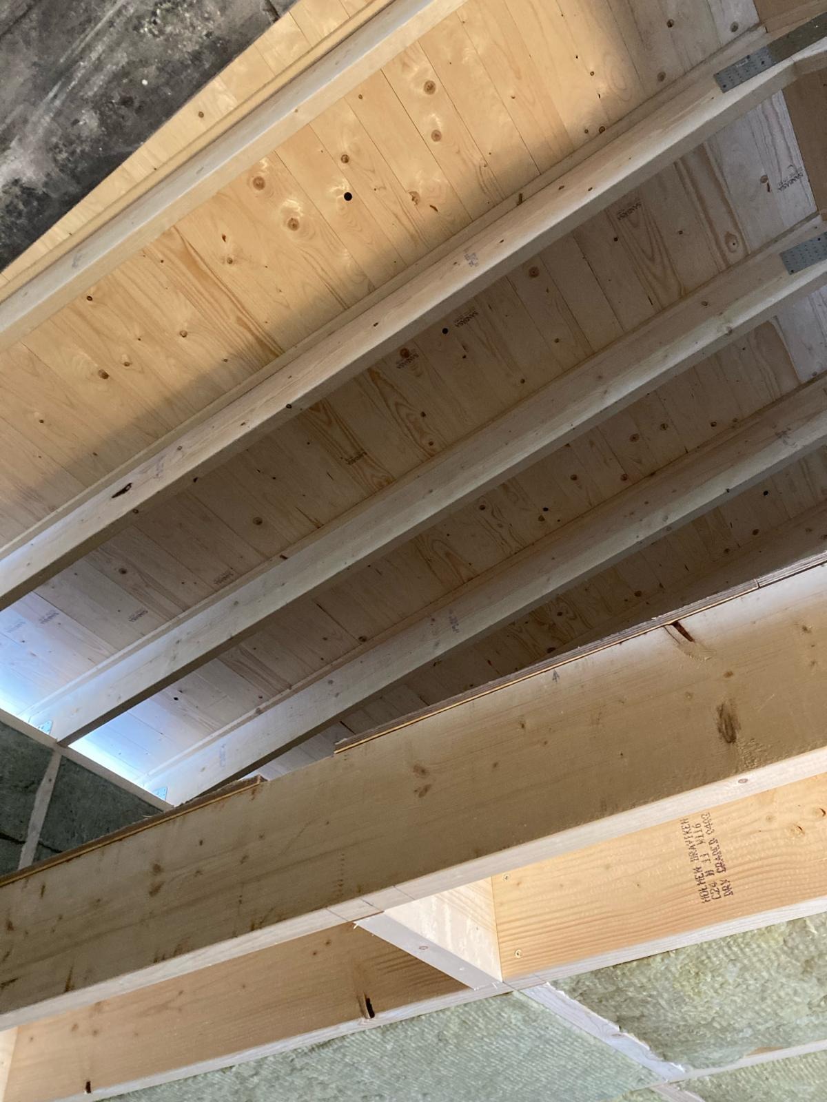 Konstrukcja drewniana poddasza z widoczną izolacją z wełny mineralnej, surowe deski stropowe, widok z dołu.
