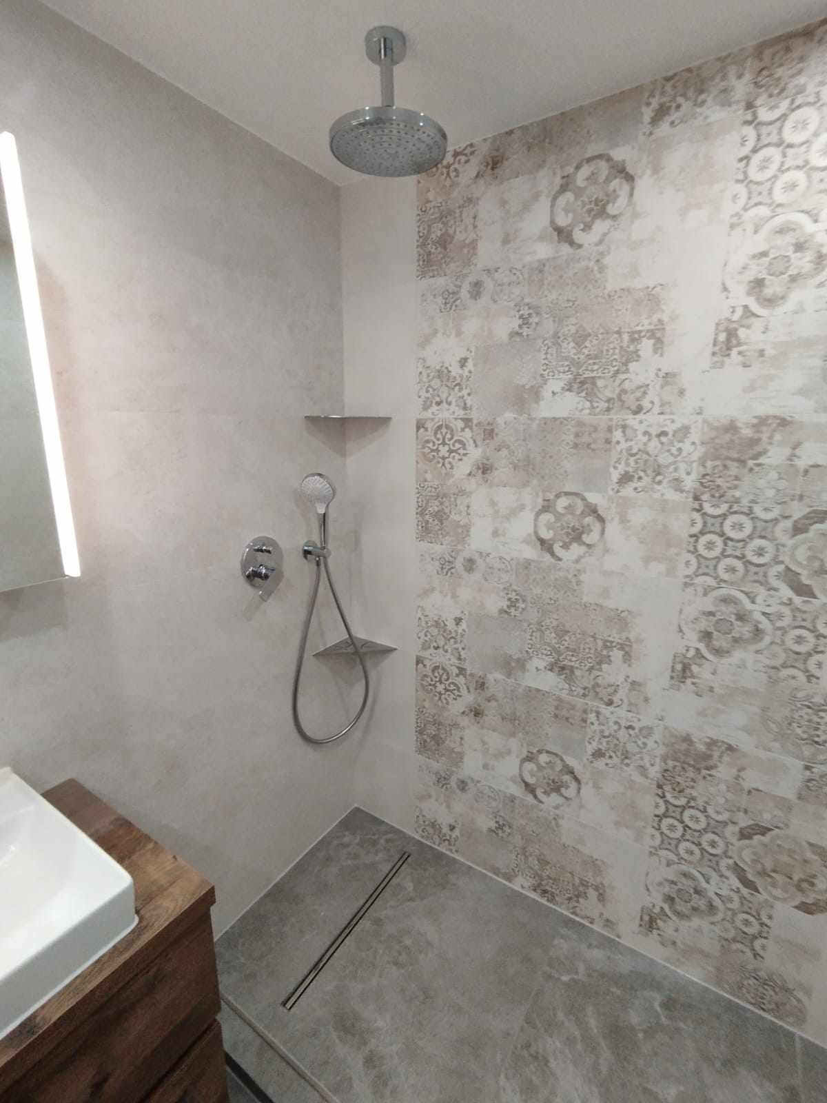 Nowoczesna kabina prysznicowa z deszczownicą, wyłożona płytkami w stylu patchwork, z odpływem liniowym w szarej posadzce.