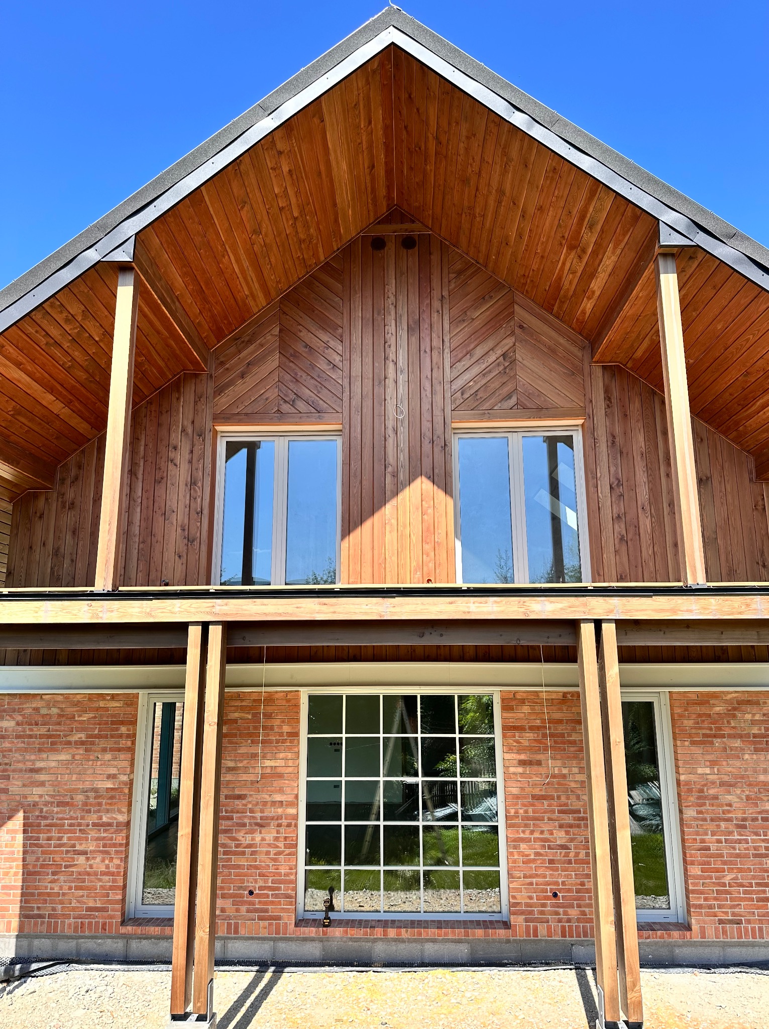 Dwukondygnacyjny budynek z czerwonej cegły i drewnianą elewacją, widoczne okna i drewniane kolumny podtrzymujące konstrukcję dachu.