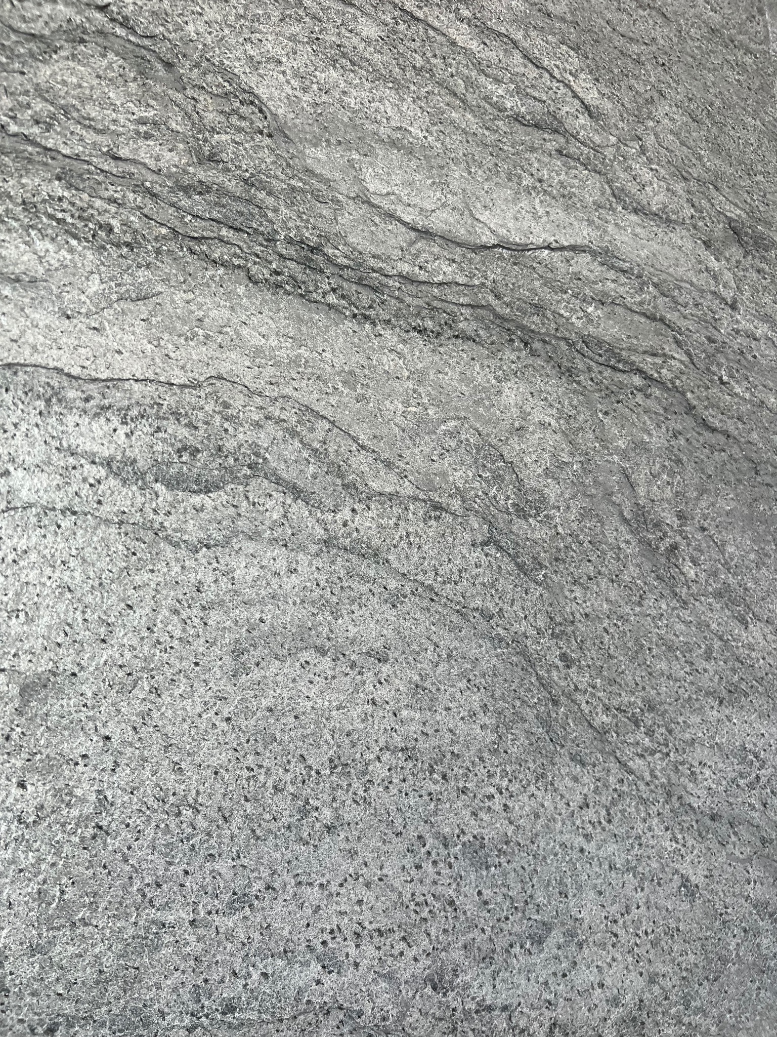 Szczegółowe ujęcie szarej, wzorzystej płytki z wyraźną, naturalną strukturą kamienia i delikatnymi, ciemniejszymi żyłkami.