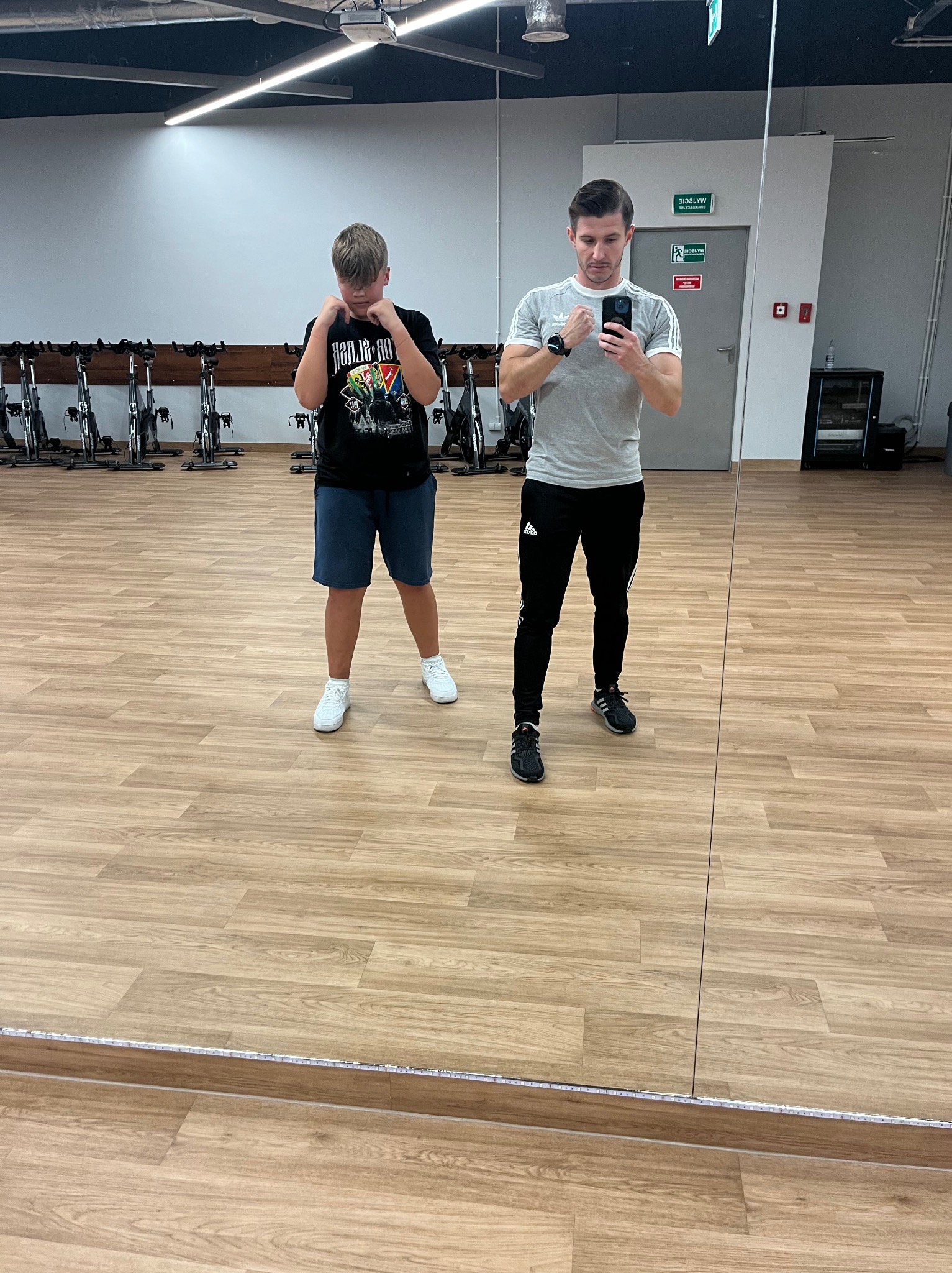 Trener personalny robi selfie z nastolatkiem w pozycji bokserskiej w siłowni z podłogą imitującą drewno