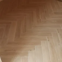 Ułożona pod kątem jasna podłoga z paneli imitujących drewno, widok na drewnianą boazerię ścienną i fragment ubrania wiszącego w rogu.