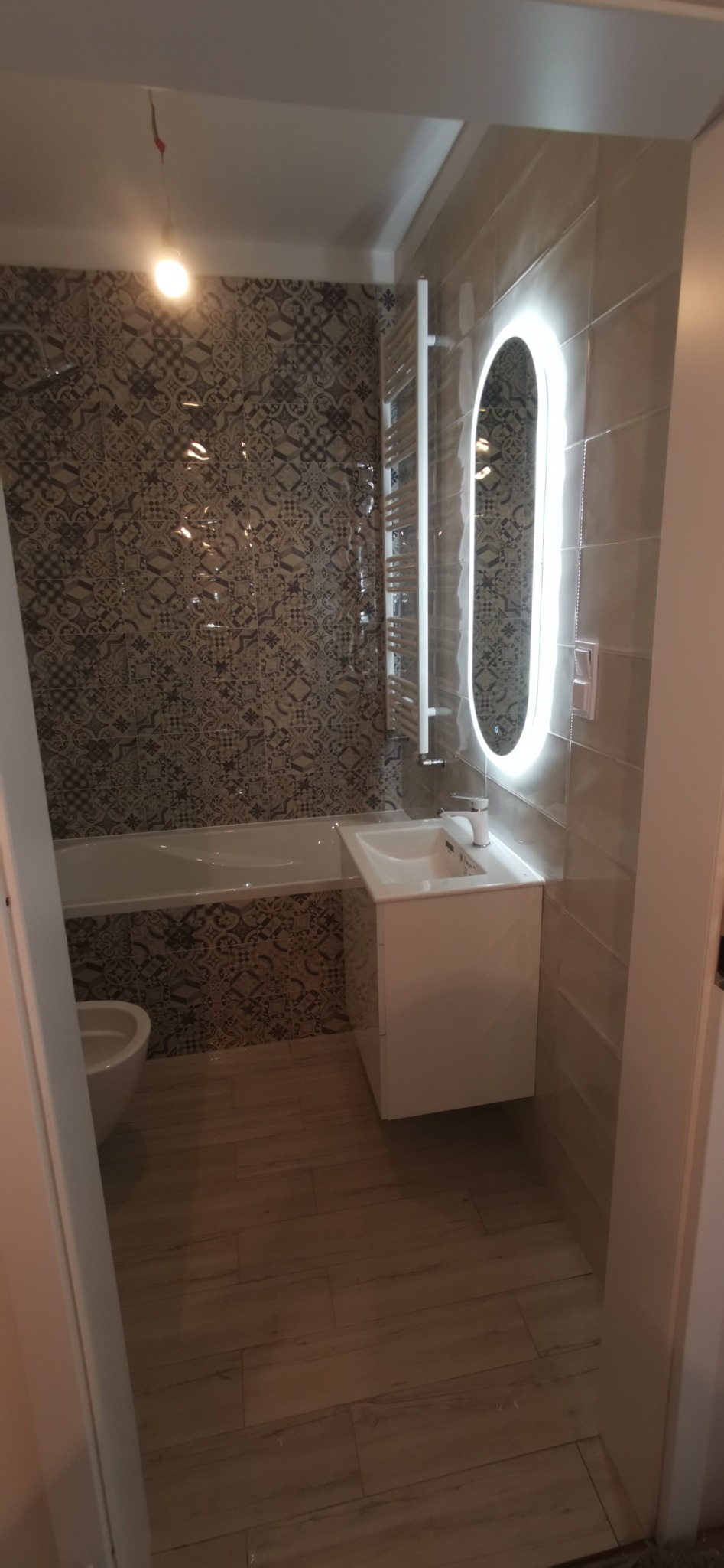 Nowoczesna łazienka z wanną obudowaną płytkami w marokańskie wzory, umywalką na szafce, podświetlanym lustrem i grzejnikiem drabinkowym.