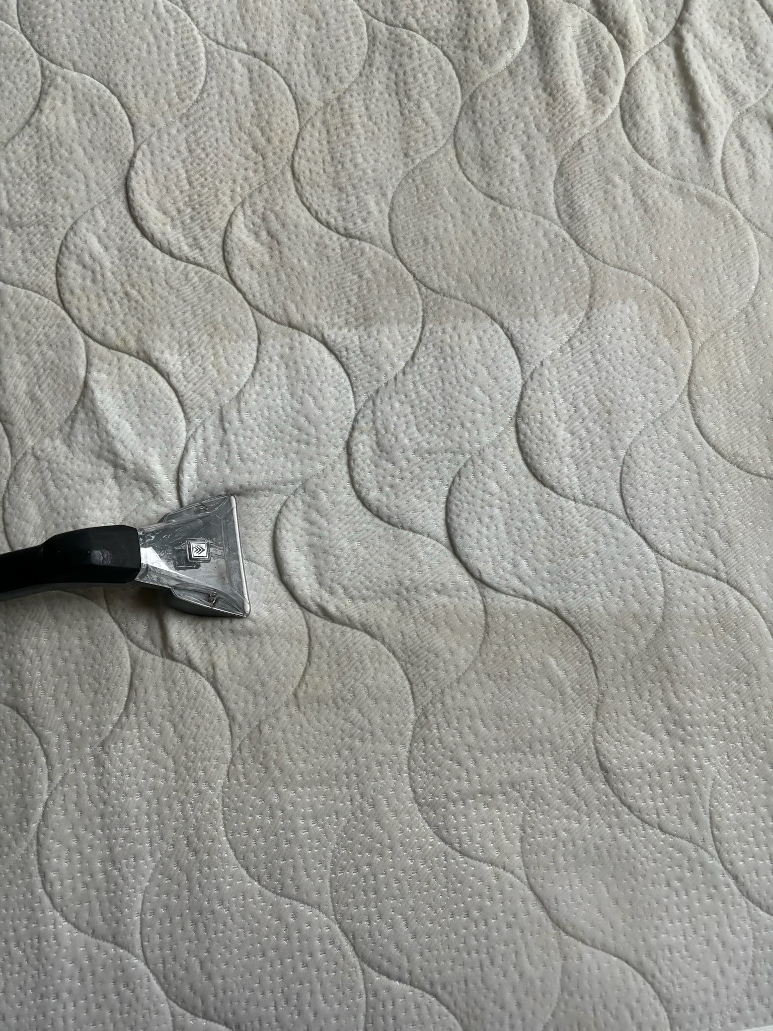 Czyszczenie materaca: dysza urządzenia ekstrakcyjnego na powierzchni materaca z widocznym wzorem pikowania i plamami wilgoci.