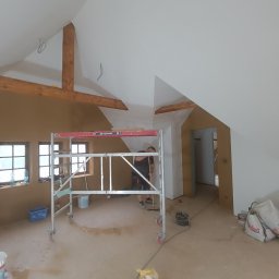 Piter HOME - Poddasze w trakcie prac. Widoczny fragment rusztowania, otynkowana ściana w kolorze piaskowym oraz pomalowany na biało sufit ze skośnymi belkami.